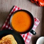 A black mug containing roasted red bell pepper soup served with toasted bread for dinner.