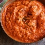 closeup shot of flavorful onion tomato chutney in a copper bowl with a spoon.