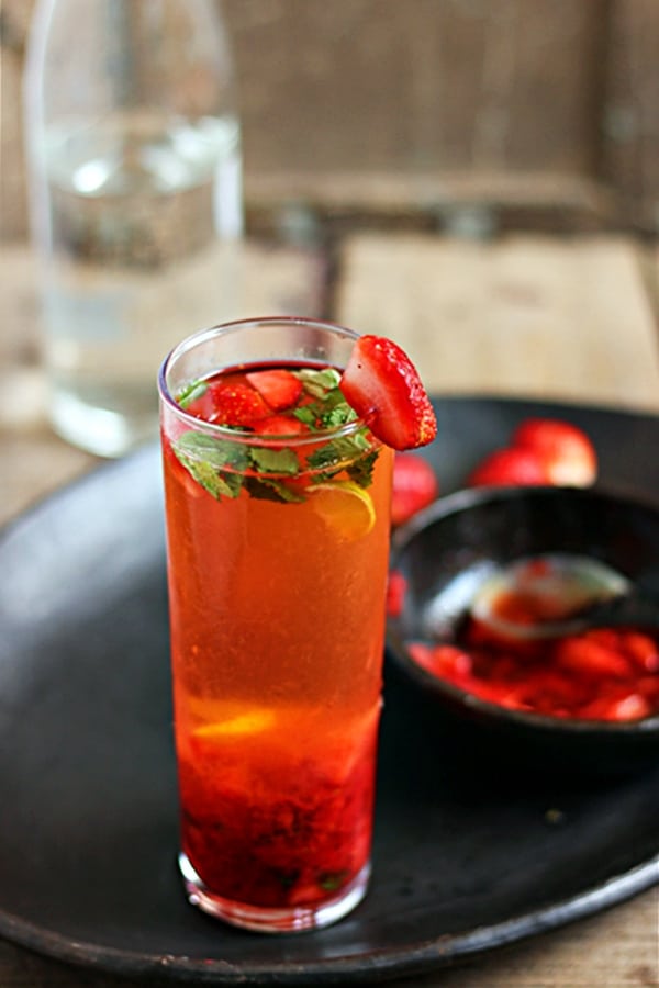 Fresh Strawberry Mojito served in a tall glass. In the background is some fresh strawberry slurry for making more mojito.