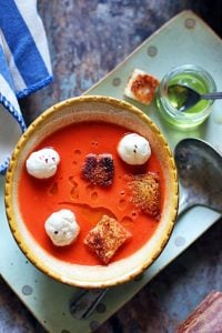 a bowl of homemade tomato soup served with croutons with more olive oil and a spoon in the tray