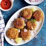 overhead shot of crispy vegan aloo tikki served with red chutney, chopped onions in ceramic plates