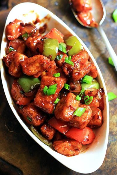 resraurant style chilli paneer served in a oval ceramic dish with a spoon