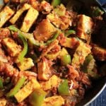 restaurant style kadai paneer served in a copper pan with a spoon.