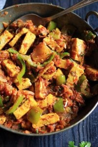 restaurant style kadai paneer served in a copper pan with a spoon.