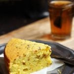 A slice of eggless mawa cake served in a metal plate with black tea