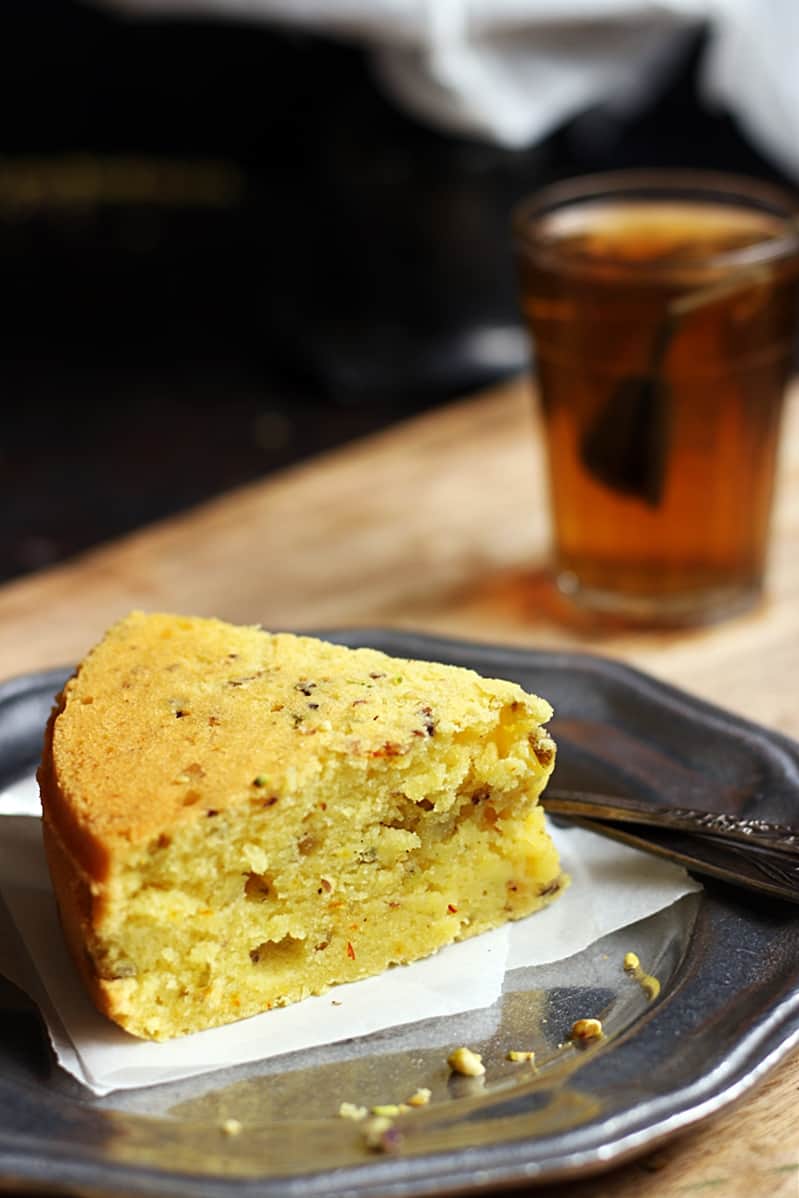 A slice of eggless mawa cake served in a metal plate with black tea