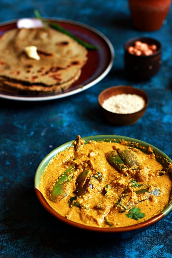 Tasty bharli vangi- Indian eggplant curry served in a two toned bowl with rotis and butter.