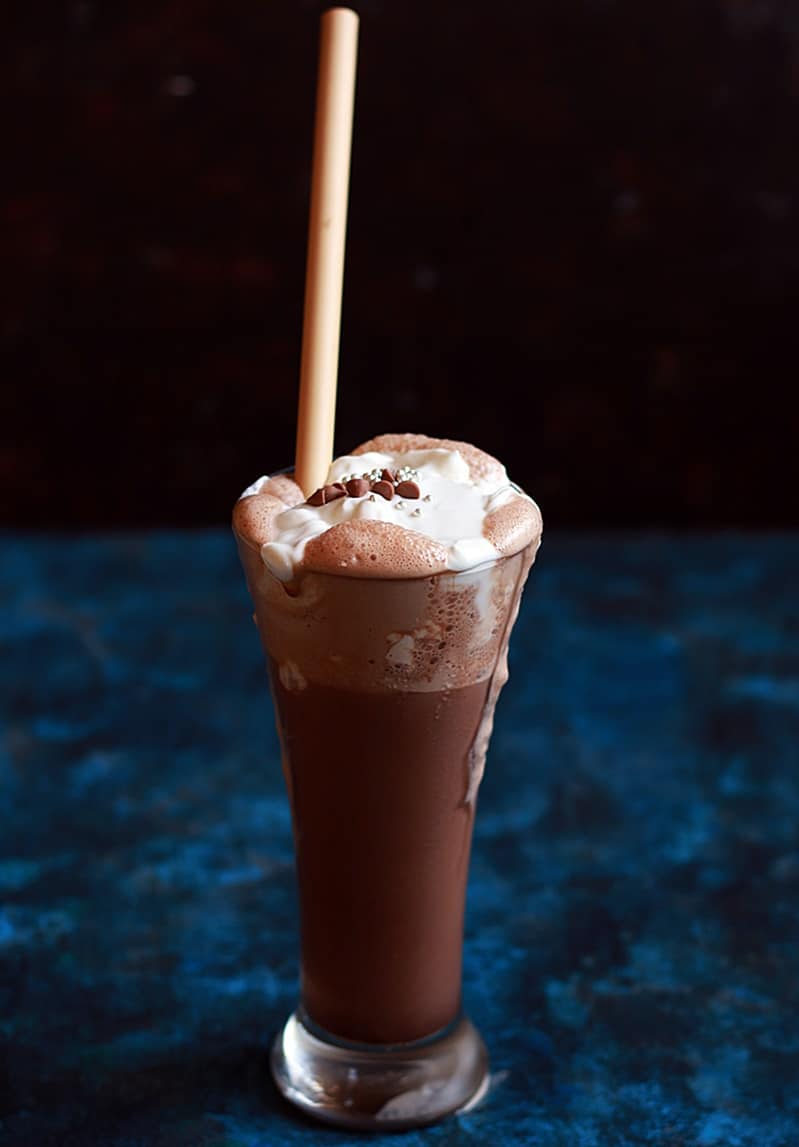 A tall glass of chocolate shake served with a bamboo straw