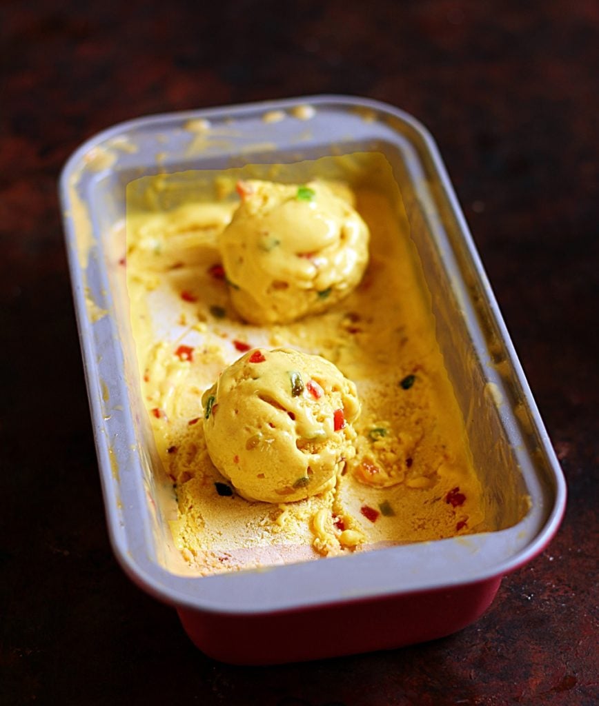 Homemade mango ice cream in a tub with two scoops scooped out