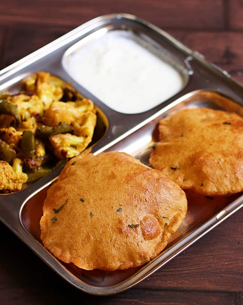 A shot of aloo puri or potati poori served in a segmented plate with curd and cauliflower stir fry for breakfast