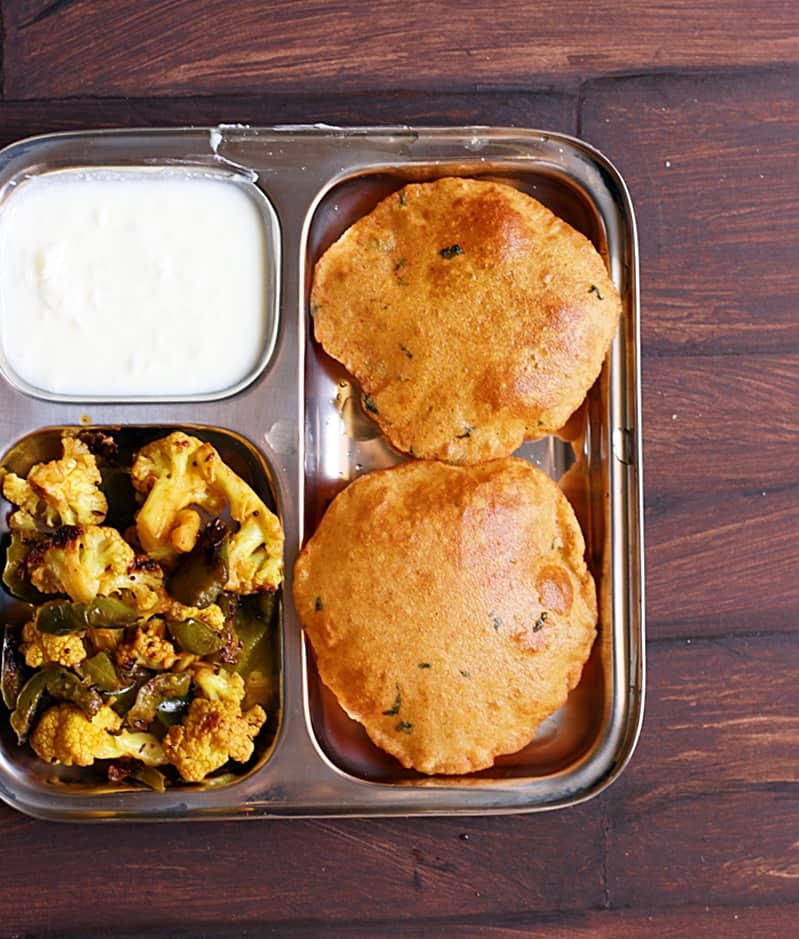 Overhead shot of aloo puri served with cauliflower and curd in a segmented plate.