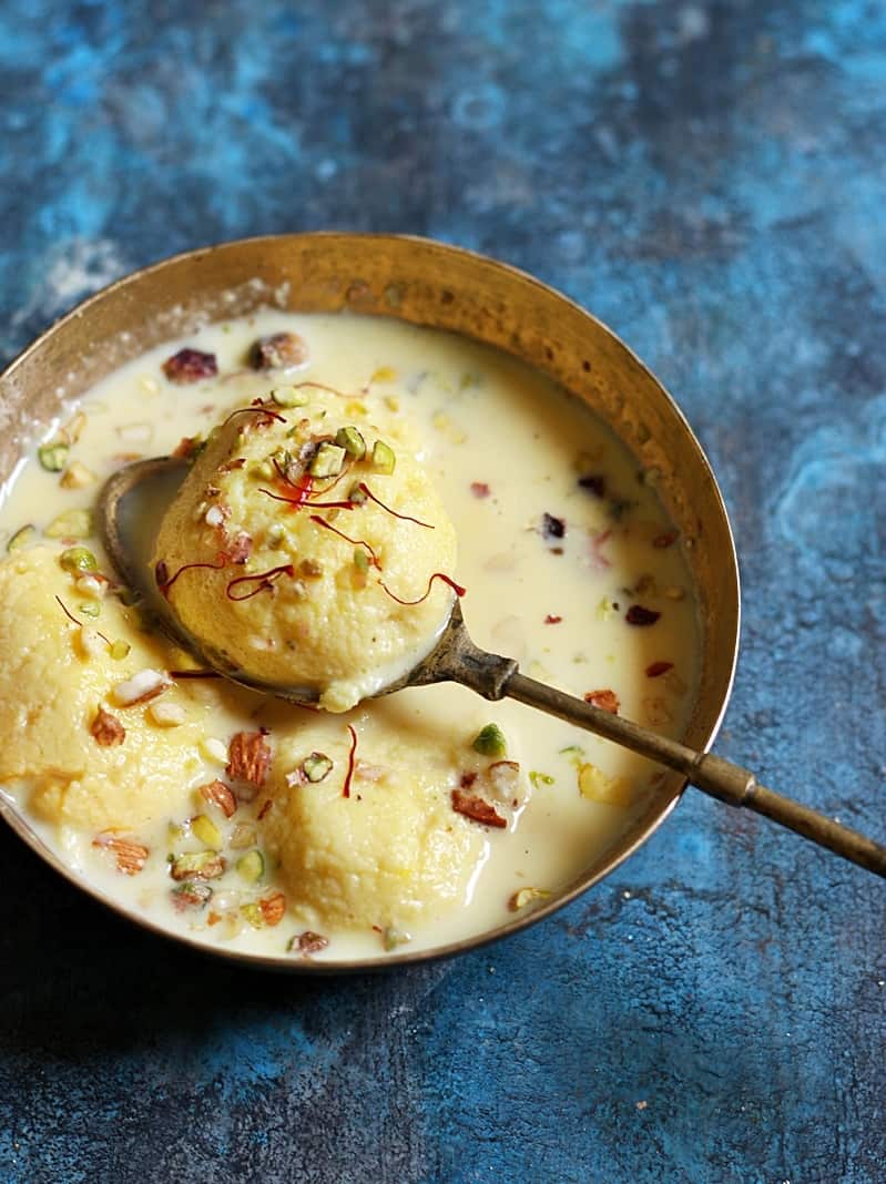 chilled rasmalai garnished with nuts and saffron served in copper bowl with a spoon.