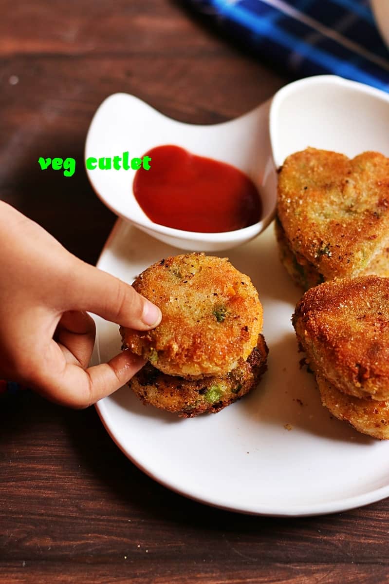 Veg cutlets served in a white plate with sauce being picked up for eating