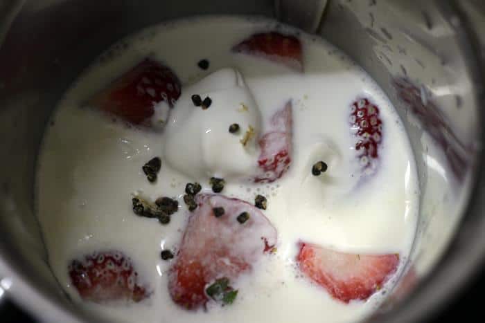 cubed berries, yogurt, cardamom pods and sugar in a blender jar for making a simple strawberry smoothie recipe