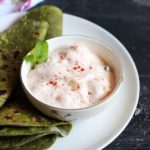 Aloo raita garnished with mint leaves served in a small bowl as side dish for palak paratha
