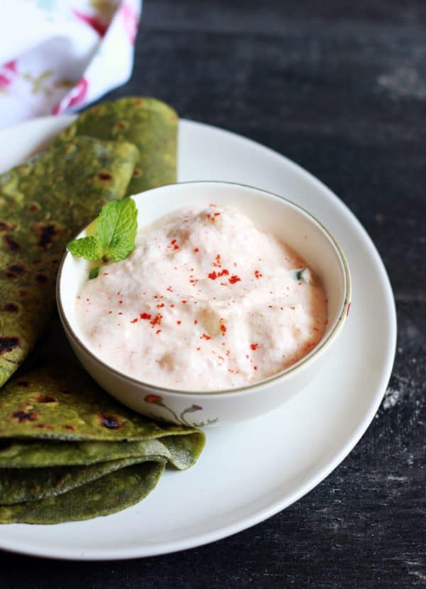 Aloo raita garnished with mint leaves served in a small bowl as side dish for palak paratha 