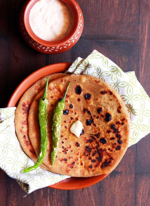 tasty paneer paratha served on bron plate with fried chilies, butter and thick curd for breakfast!