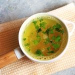 Quick and tasty lemon rasam garnished with cilantro leaves and served on a white soup bowl.