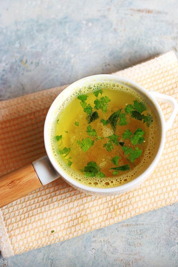 Quick and tasty lemon rasam garnished with cilantro leaves and served on a white soup bowl.