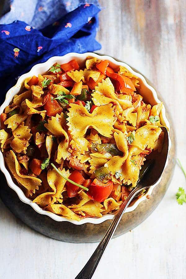 Indian style masala pasta served in a shallow white dish with a metal spoon