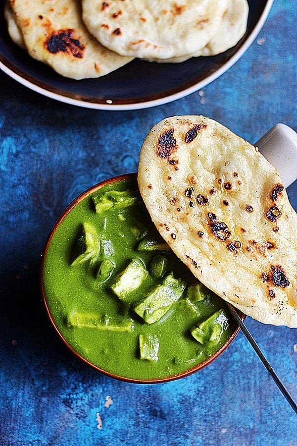 palak paneer served in a bowl with naan on top and a spoon.