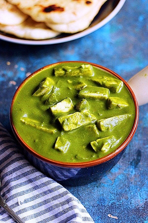 palak paneer served in a ceramic bowl with naan bread in the background.
