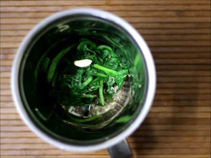 Blending blanched spinach leaves with ginger garlic and green chili in a mixer grinder jar