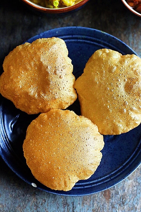 crispy puffed golden pooris served in a ceramic blute plate with potato masala 