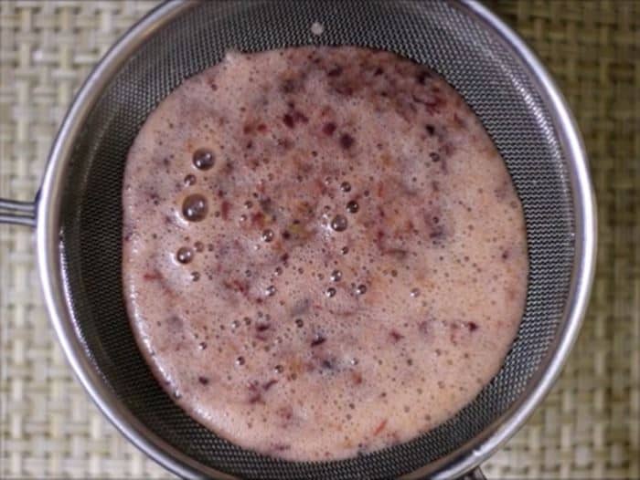 Straining the blended grape juice through a metal strainer