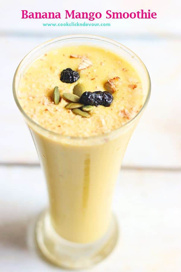 Banana mango smoothie garnished with pumpkin seeds and dried berries, served in a glass