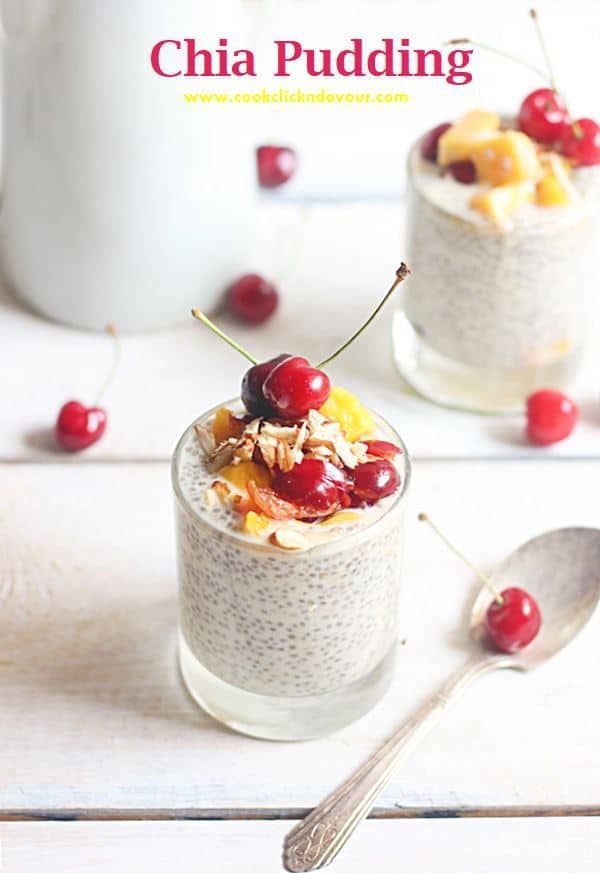 healthy vanilla chia pudding served in a glass tumbler topped with nuts and cherries. There is one more serving of same pudding in the background