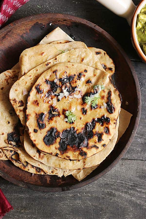 Homemade soft tandoori roti stacked in a wooden plate.