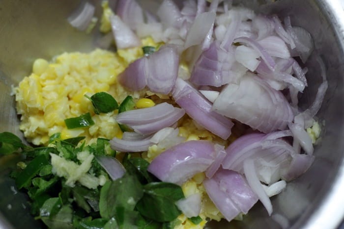 Mixing chopped onions, curry leaves and green chilies with pulsed sweet corn
