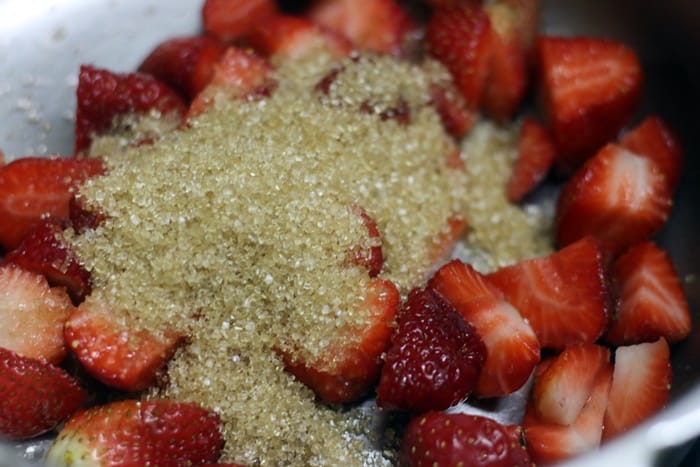 Adding sugar and chopped berries in a pan 