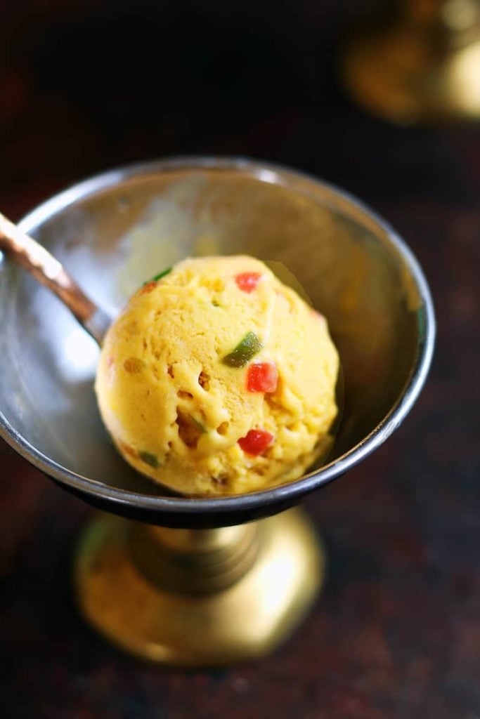 A perfect scoop of homemade mango ice cream in a copper ice cream bowl with a spoon