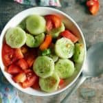 overhead shot of fresh cucumber tomato salad with lemon dressing served in a white and blue bowl.