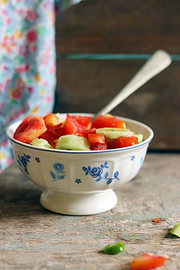 Cucumber tomato salad served in white and blue footed bowl with a spoon.