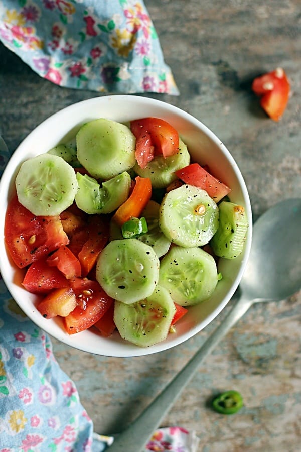 overhead shot of fresh cucumber tomato salad with lemon dressing served in a white and blue bowl.