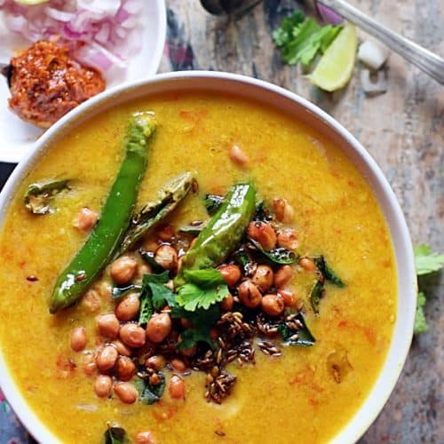Overview shot of dal dhokli served with peanuts garnish, mango pickle and raw onions