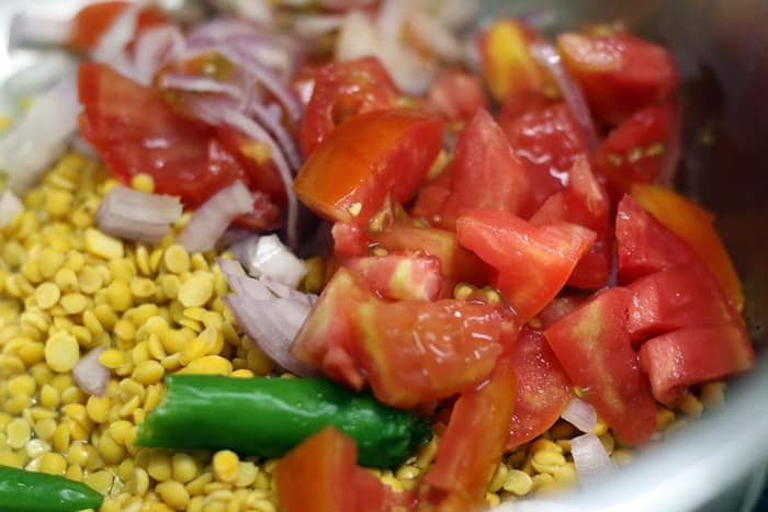 Dal, onion, tomatoes, green chilies added to the pressure cooker to make dal for dal dhokli recipe