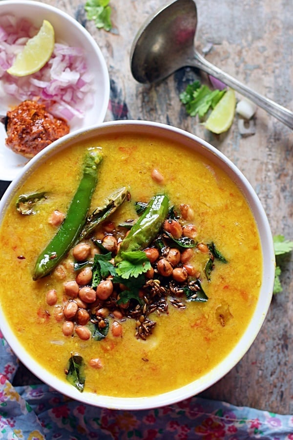 Overhead shot of dal dhokli served with peanuts garnish, mango pickle and raw onions