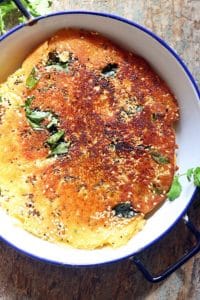 Handvo made and served in a enamel pan with sesame seeds and curry leaves garnishing