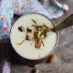 Overhead shot of sweet lassi garnished wit nuts, saffron and served with a long spoon