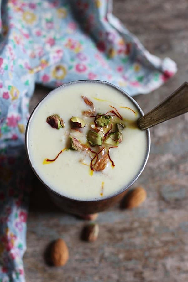 Overhead shot of sweet lassi garnished wit nuts, saffron and served with a long spoon