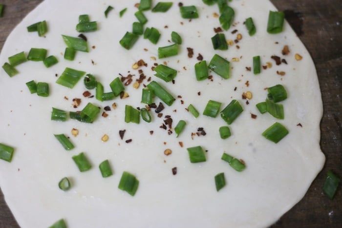 Chopped scallions and chili flakes sprinkled on rolled pancake dough