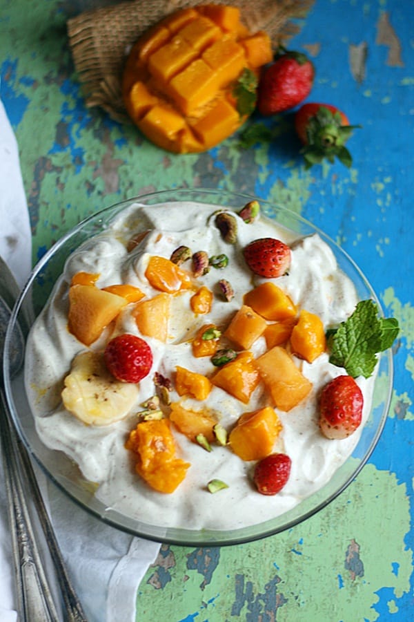 A bowl of chilled fruit cream with some cut fruits in background