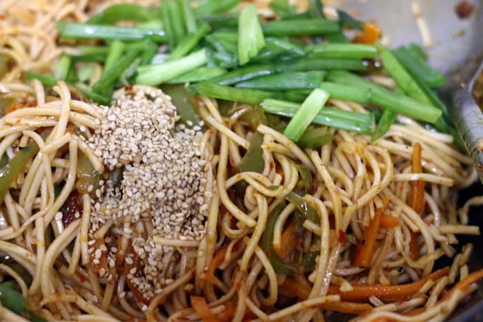Schezwan noodles topped with sesame seeds and spring onion greens