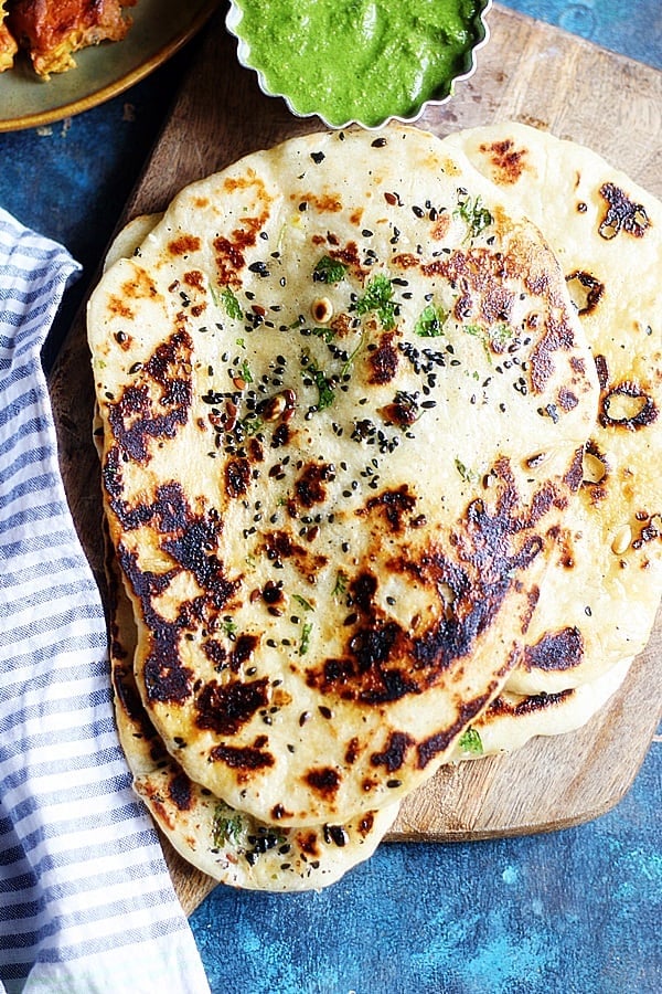 Stack of homemade made vegan naan placed on wooden serving board.