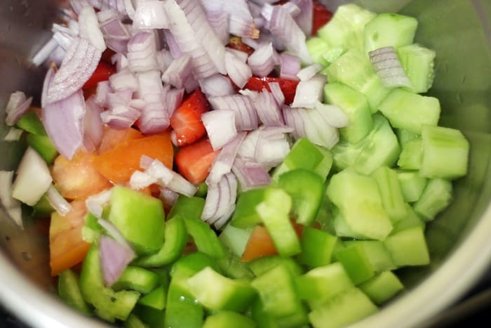 Chopped onions, cucumber, tomatoes and strawberries in a mixing bowl