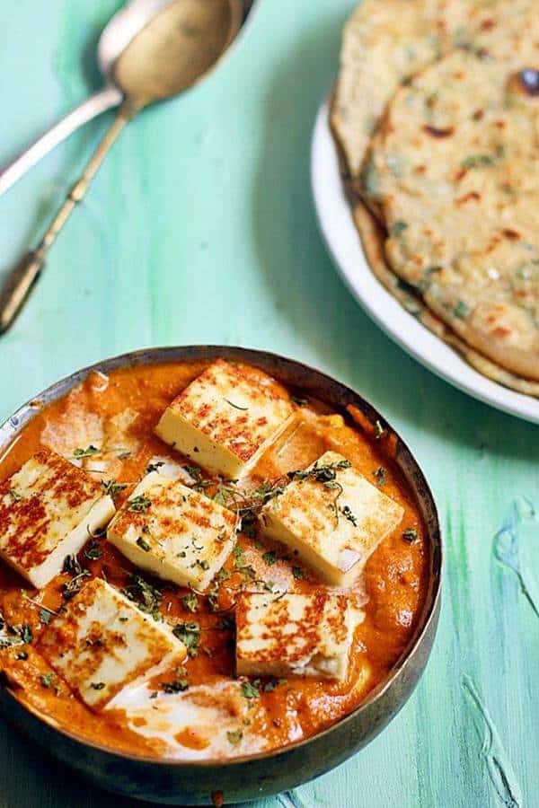 close up shot of paneer butter masala serve with naan in the background